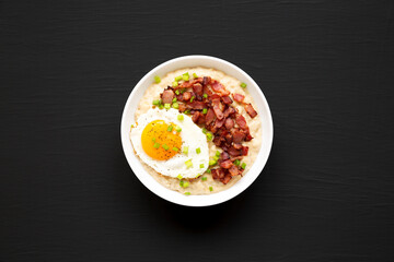 Homemade Cheesy Bacon Savory Oatmeal Bowl on a black background, top view. Overhead, from above, flat lay.