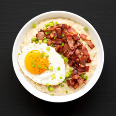 Homemade Cheesy Bacon Savory Oatmeal Bowl on a black surface, top view. Overhead, from above, flat lay.