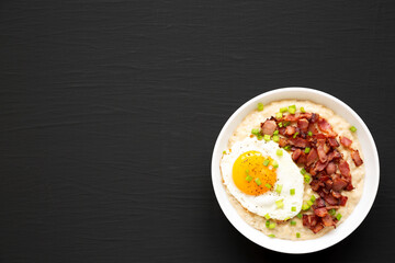 Homemade Cheesy Bacon Savory Oatmeal Bowl on a black background, top view. Overhead, from above, flat lay. Space for text.