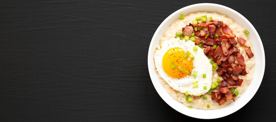 Homemade Cheesy Bacon Savory Oatmeal Bowl on a black surface, top view. Overhead, from above, flat lay. Copy space.