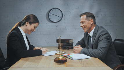  insurance agent writing on document near colleague, scales and notebook