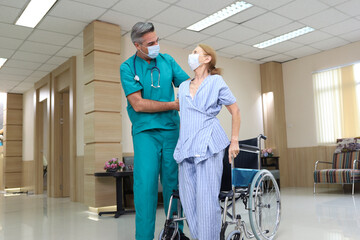 Doctor or assistance staff wear face mask and help or assist an elder patient woman while try to standing or walking or sitting on wheelchair in the hospital, eldercare concept