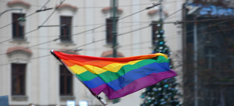 Rainbow flag symbolizes LGBT+ groups waves against Christmas tree in urban area