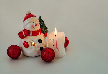 Snowman next to some red Christmas balls and looking at a lit candle		