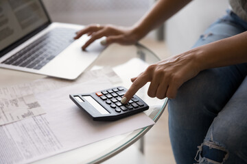 Close up young woman using calculator and online banking application on computer managing monthly...