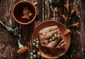 pie and herbal tea in an orange mug on a wooden table. berries, herbs, flowers and tea on a brown wooden table. summer still life with herbs, delicious pie and flowers on the kitchen table