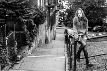 Obraz premium Young long-haired girl sitting on the parapet in the old town. Black and white photo.