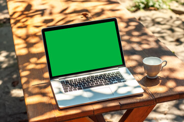 View on a laptop pc with a green screen and a coffee mug on a table in the garden
