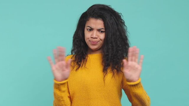 Confused disgusted african american woman 20s in yellow sweater isolated on blue background in studio. People lifestyle concept. Say no with finger gesture showing stop gesture with palm crossed hands