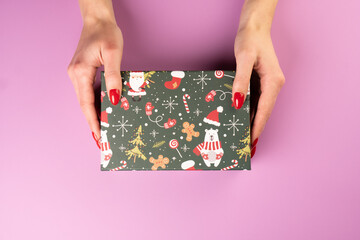 Fototapeta premium Woman hands holding christmas box or gift box on pink pastel table top view. 
