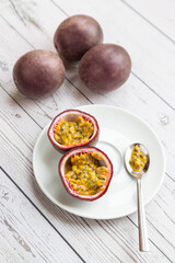passion fruit in a white plate on a white wooden table, one is cut and ready-to-eat with a spoon - 396087952