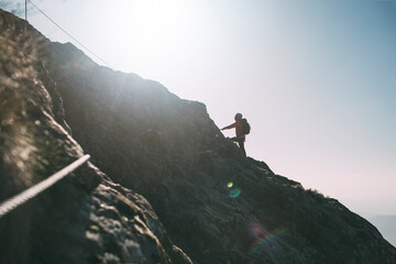 Mountaineer with backpack climbing along a via ferrata