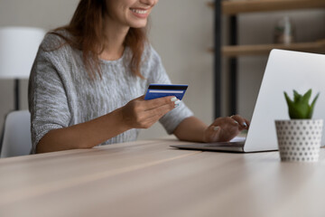 Close up smiling female shopper using bank credit card involved in purchasing goods or services in internet store, happy young woman entering payment information in computer shopping application.
