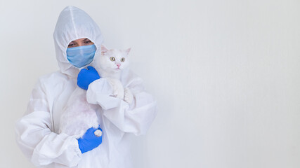 A woman in a protective suit with gloves and a mask is holding a white cat. Doctor tests pets for coronavirus