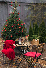 Street cafe under Christmas tree with red decor outdoor. Wooden tables and chairs with warm plaid at winter market in garden. Cozy festive and New Year atmosphere in Europe. film effect.