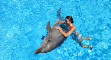 Happy woman swims with cute dolphin in blue water. Dolphin therapy concept - Powered by Adobe