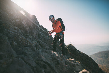 Mountaineer using climbing equipment to climb rocky mountain summit