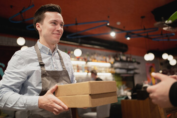 Courier delivery of food from the restaurant to the client's home, high-quality packaging in paper boxes. Passes the parcel to the courier and asks them to deliver food quickly.