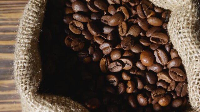 Rotating bag full of roasted coffee beans on table, closeup