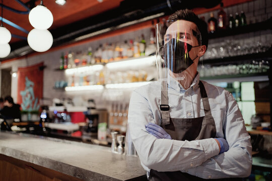 holding a pot of hot coffee. It is worth waiting for new customers to work in a new small cafe. waiter male mask from the early stages of the pandemic virus on the face and antibacterial glass.