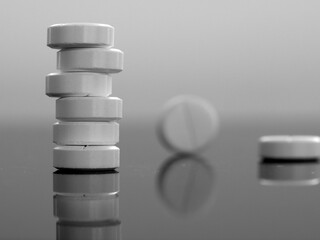 Black and white monochrome background with round pills close-up. The pills are stacked and individually on a black mirror surface. Medical background with medicines.