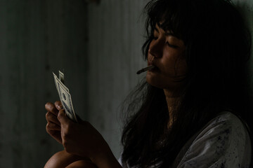 Asian woman sitting with a cigarette counting dollars Inside the old, shabby, dark room, the atmosphere is scary. under the concept of sex crimes and drugs