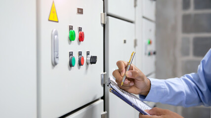 Close-up hand of electrical engineer checking the electric current voltage and overload at front of load center cabinet or consumer unit for maintenance in main power distribution system room.