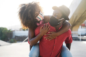 African couple having fun outdoor wearing safety masks during Coronavirus outbreak - Covid 19...