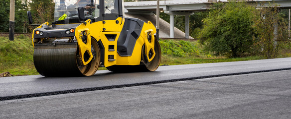 Asphalt road roller with heavy vibration roller compactor press new hot asphalt on the roadway on a road construction site. Heavy Vibration roller at asphalt pavement working. Repairing.