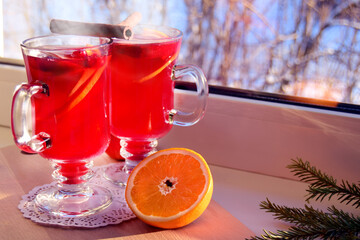 Mulled wine with spices and orange on a wooden board standing on a light windowsill. Christmas...