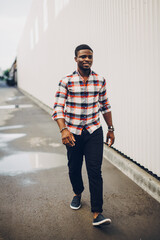 Portrait of a happy black guy in a plaid shirt walking in the city