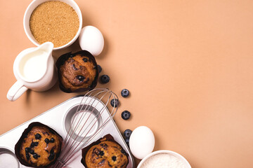 Homemade Blueberry Muffins with Berries Baking Dish Milk Eggs Sugar Flour Ingredients for Baking Muffins Light Brown Background Top View Horizontal Copy Space