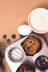Homemade Blueberry Muffins with Berries Baking Dish Milk Eggs Sugar Flour Ingredients for Baking Muffins Light Brown Background Top View Vertical Copy Space
