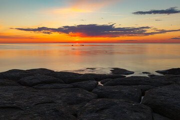 Beautiful colorfull sunset over the sea shore with rocks under shallow water