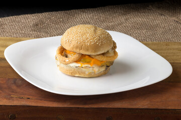 Gourmet hamburger with cheddar cheese and bacon on white plate on top of the board