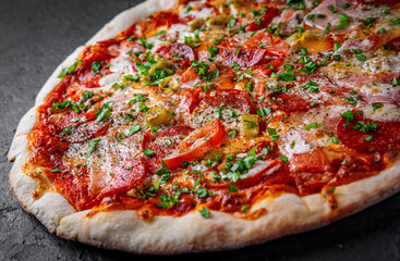 Pizza with Mozzarella cheese, ham, tomato sauce, pepper, salami. Italian pizza on Dark grey black slate background