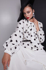 Woman with black hat wide white trousers and polka dot free shirt posing for fashion on a white and black background
