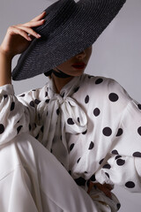 Woman with black hat wide white trousers and polka dot free shirt posing for fashion on a white and black background - 396099754