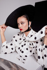 Woman with black hat wide white trousers and polka dot free shirt posing for fashion on a white and black background - 396099781