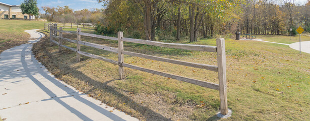 Fototapeta premium Panoramic long curved concrete pathway with wooden fence colorful fall foliage at park in Texas, USA
