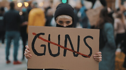 No guns. Young woman with face mask holding banner against gun violence. Demonstration and revolution concept. High quality photo