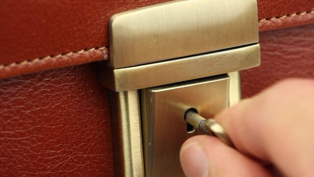 human several times tries to open lock on gold buckle of expensive or luxury red leather briefcase, small key sticks, lock is broken or the mechanism is defective, close-up macro view