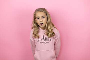 Young beautiful child girl standing over isolated pink background afraid and shocked with surprise and amazed expression, fear and excited face.