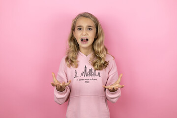 Young beautiful child girl standing over isolated pink background crazy and mad shouting and yelling with aggressive expression and arms raised. Frustration concept.