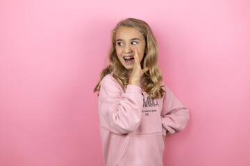 Fototapeta premium Young beautiful child girl standing over isolated pink background with her hand on mouth telling secret rumor, whispering malicious talk conversation