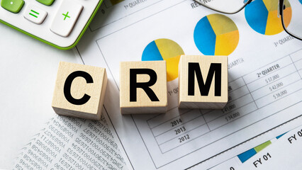 The inscription on the cubes, the word CRM on the cubes of wooden texture. View from above. Desktop with documents. An inscription on a financial, business or economic theme.