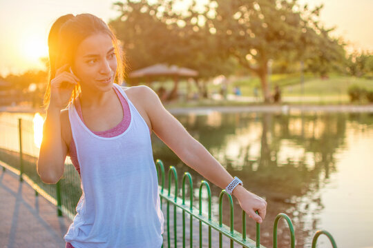 Beautiful young woman in sportswear listening to music using wireless earbuds in the park