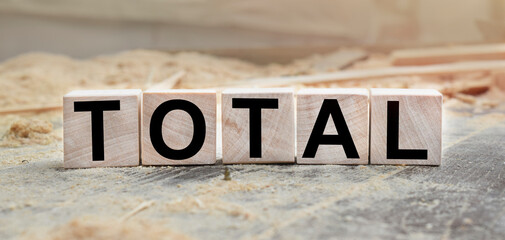 The word TOTAL is written on wooden cubes. Wooden cubes lie on the table with sawdust and wooden blocks. Designed to promote your business. Marketing concept.