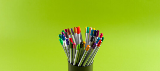 A set of colored pencils for creativity at home in a cup on a light green background, side view. Space for text, wide format.
