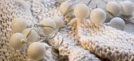 New Year's glowing lights on a white knitted scarf. Winter Christmas decor. Festive atmosphere. Warm colors, soft focus.